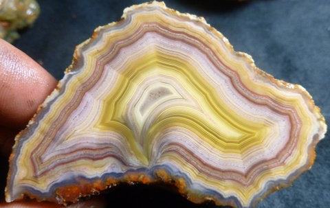 Close-up of a multicolored agate stone held between fingers on a dark surface.